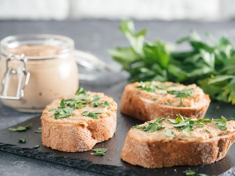 Close up view of slice bread with homemade turkey pate and fresh green parsley on black slate board over gray concrete background, Copy space. Shallow DOF