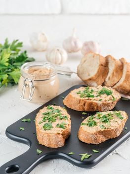 Close up view of slice bread with homemade turkey pate and fresh green parsley on black kutting board over white concrete background, Copy space.