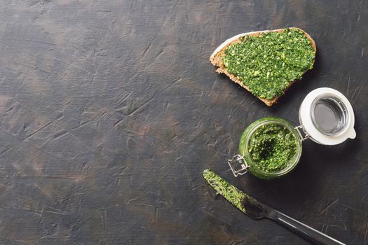 whole grain rye bread with fresh basil pesto sauce on dark concrete background. Top view or flat-lay. Copy space.