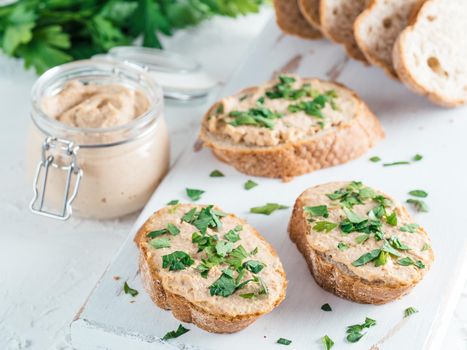 Close up view of slice bread with homemade turkey pate and fresh green parsley on white rustic kutting board over white concrete background, Shallow DOF. Selective focus