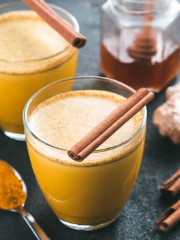 Healthy drink golden turmeric latte in glass.Gold milk with turmeric,ginger root,cinnamon sticks,dried turmeric powder and honey over black cement background.Detox turmeric tea and ingredients.Toned