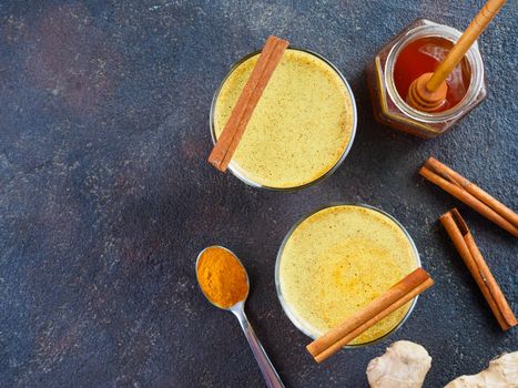 Healthy drink golden turmeric latte in glass.Gold milk with turmeric,ginger root,cinnamon sticks,turmeric powder and honey on black background.Detox turmeric tea and ingredients. Copy space. Top view