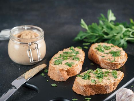 Close up view of slice bread with homemade turkey pate and fresh green parsley on black kutting board over black cement background, Copy space.