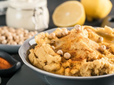Homemade hummus with olive oil in gray bowl and ingredients. Traditional middle eastern appetizer hummus on gray background - healthy vegan paste snack. Vegetarian diet,nutrition protein food concept