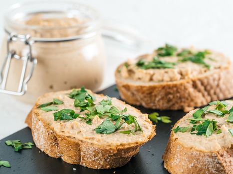 Close up view of slice bread with homemade turkey pate and fresh green parsley on black kutting board over white concrete background, Shallow DOF. Selective focus