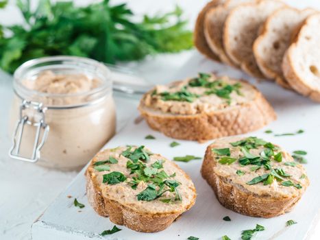 Close up view of slice bread with homemade turkey pate and fresh green parsley on white rustic kutting board over white concrete background, Shallow DOF. Selective focus