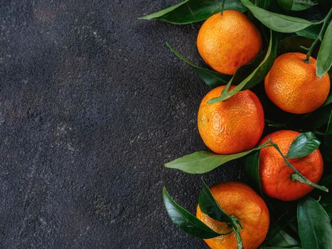 Tangerines, oranges, mandarins, clementines, citrus fruits with leaves on black cement background. Top view or flat-lay. Copy space.