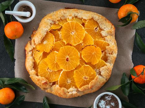 Top view of caraway and orange tart on baking paper over black cement background. Winter season and christmas ideas recipe - tart with caraway pastry and oranges, mandarines or tangerines.
