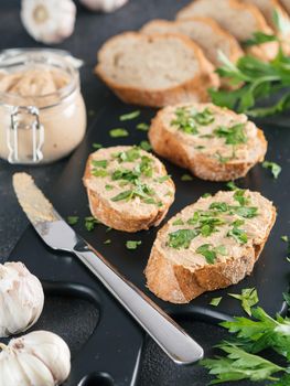 Close up view of slice bread with homemade turkey pate and fresh green parsley on black kutting board over black cement background,