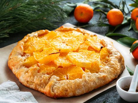Close up view of caraway and orange tart on baking paper over black cement background. Winter season and christmas ideas recipe - tart with caraway pastry and oranges, mandarines or tangerines.
