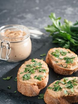 Close up view of slice bread with homemade turkey pate and fresh green parsley on black slate board over gray concrete background, Copy space. Shallow DOF