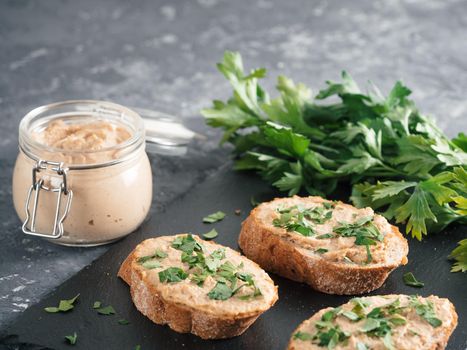 Close up view of slice bread with homemade turkey pate and fresh green parsley on black slate board over gray concrete background, Copy space. Shallow DOF