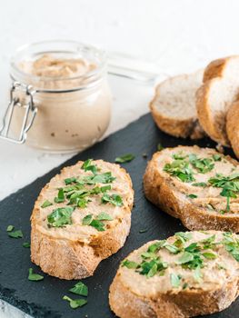 Close up view of slice bread with homemade turkey pate and fresh green parsley on black kutting board over white concrete background, Copy space.