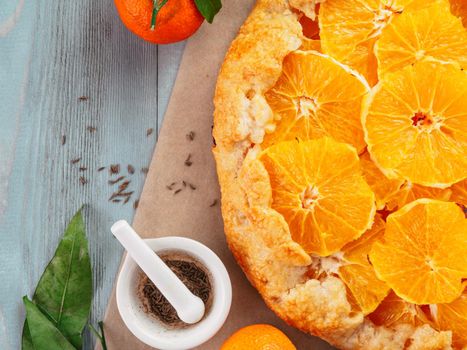 Top view of caraway and orange tart on baking paper over gray wooden table with copy space.Winter season and christmas ideas recipe-tart with caraway pastry and oranges, mandarines or tangerines