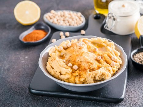 Homemade hummus with olive oil in gray bowl and ingredients. Traditional middle eastern appetizer hummus on gray background - healthy vegan paste snack. Vegetarian diet,nutrition protein food concept