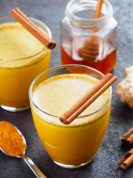 Healthy drink golden turmeric latte in glass.Gold milk with turmeric,ginger root,cinnamon sticks,dried turmeric powder and honey over black cement background.Detox turmeric tea and ingredients.