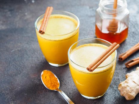 Healthy drink golden turmeric latte in glass.Gold milk with turmeric,ginger root,cinnamon sticks,turmeric powder and honey over black cement background.Detox turmeric tea and ingredients.Copyspace