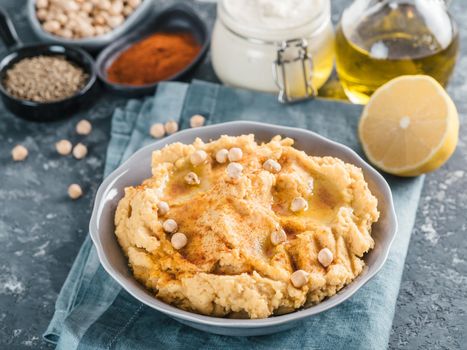 Homemade hummus with olive oil in gray bowl and ingredients. Traditional middle eastern appetizer hummus on gray background - healthy vegan paste snack. Vegetarian diet,nutrition protein food concept