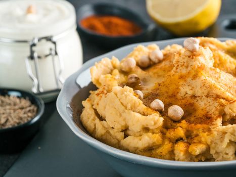 Homemade hummus with olive oil in gray bowl and ingredients. Traditional middle eastern appetizer hummus on gray background - healthy vegan paste snack. Vegetarian diet,nutrition protein food concept