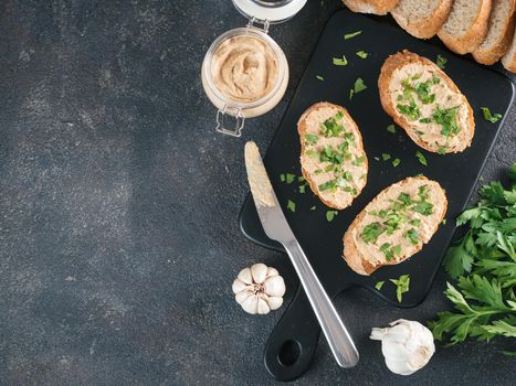 Top view of slice bread with homemade turkey pate and fresh green parsley on black kutting board over black cement background, Copy space.