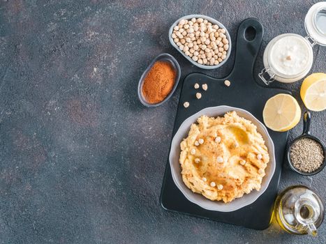 Homemade hummus in gray bowl and ingredients. Traditional middle eastern appetizer hummus on dark background - healthy vegan paste snack. Vegetarian diet,nutrition protein food concept. Copy space.