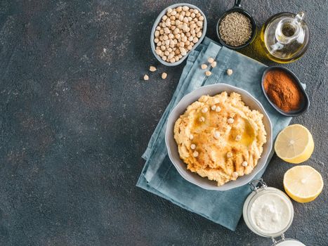 Homemade hummus in gray bowl and ingredients. Traditional middle eastern appetizer hummus on dark background - healthy vegan paste snack. Vegetarian diet,nutrition protein food concept. Copy space.