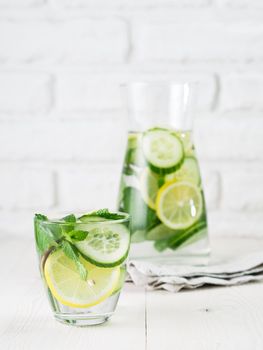 Infused detox water with cucumber, lemon and mint in glass and bottle on white table. Diet, healthy eating, weight loss concept. Copy space