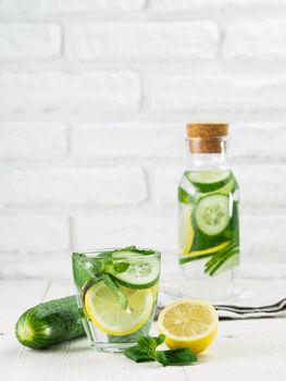 Infused detox water with cucumber, lemon and mint in glass and bottle on white table. Diet, healthy eating, weight loss concept. Copy space