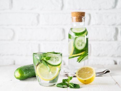 Infused detox water with cucumber, lemon and mint in glass and bottle on white table. Diet, healthy eating, weight loss concept. Copy space