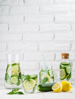 Infused detox water with cucumber, lemon and mint in different glass bottles on white table. Diet, healthy eating, weight loss concept. Copy space