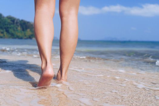 Woman feet walk slow life and relax on sand tropical beach with blue sky background. Vacation and holiday concept.
