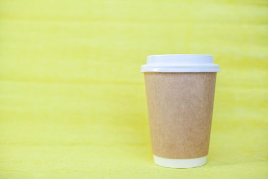 Paper cup of coffee closed with a white lid on a yellow background. There is a place for the text.