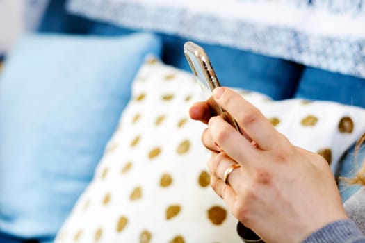 the hands of a young caucasian brunette woman while holding a smartphone typing on the touch screen. Technology and mobile connection.