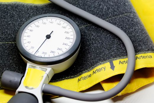 a portable sphygmomanometer resting on a yellow cuff for adults with a velcro closure. Instrument for measuring blood pressure. Graduated scale with pressure indicator. Medical instrument. Health and disease prevention