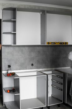 Custom kitchen cabinets installation without a furniture facades mdf. Gray modular kitchen from chipboard material on a various stages of installation in kitchen with a grey tile on floor and walls