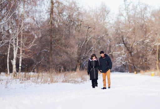 Young couple walking through the winter forest holding hands.