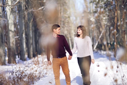 Young couple walking through the winter forest holding hands.
