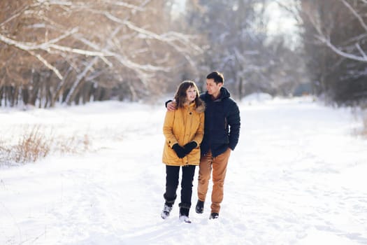 On a winter day, a young couple is walking in an embrace in the park and communicating.