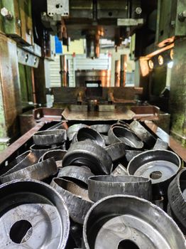 pile of stamped thick sheet black metal round parts after a hood operation in front of old blurred forming press with die tooling