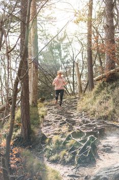 Active sporty woman listening to the music while running in autumn fall forest. Female runner training outdoor. Healthy lifestyle image of young caucasian woman jogging outside.