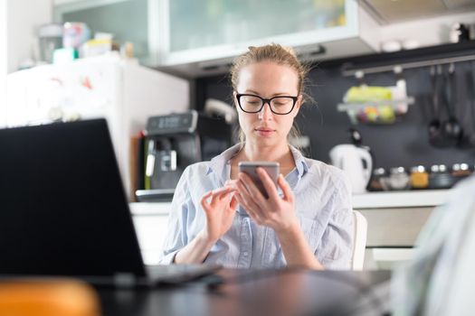 Stay at home and social distancing. Woman in her casual home clothing working remotly from kitchen dining table. Video chatting using social media with friend, family, business clients or partners.