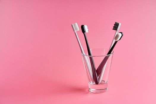 Fashionable toothbrush with soft bristles. Popular toothbrushes. Hygiene trends. Kit of toothbrushes in glass on pink background.