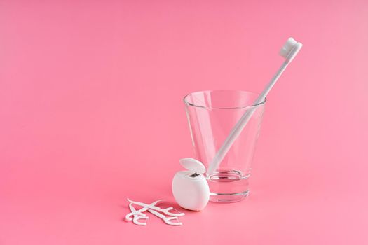 Fashionable toothbrush with soft bristles. Popular toothbrushes. Hygiene trends. Oral hygiene kit. Toothbrushes in glass, floss thread and toothpicks on a pink background.