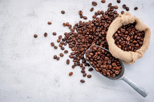 Roasted coffee beans with scoops setup on white concrete background.