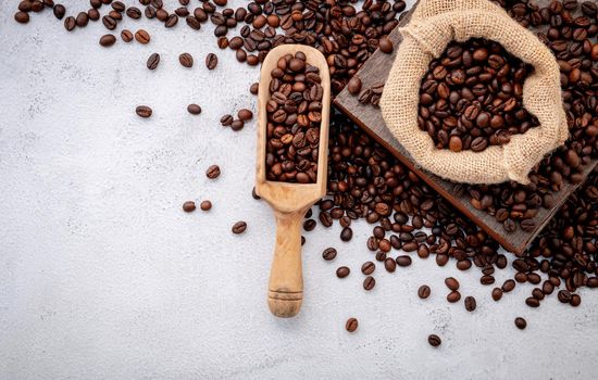 Roasted coffee beans with scoops setup on white concrete background.