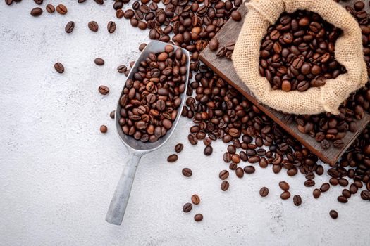 Roasted coffee beans with scoops setup on white concrete background.