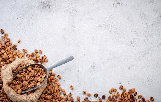 Roasted coffee beans with scoops setup on white concrete background.