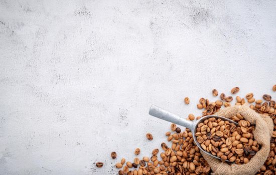 Roasted coffee beans with scoops setup on white concrete background.