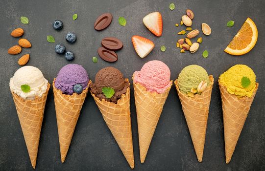 Various of ice cream flavor in cones blueberry ,pistachio ,almond ,orange and chocolate setup on dark stone background . Summer and Sweet menu concept.