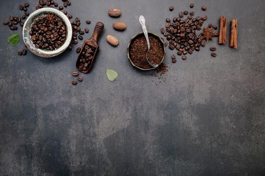 Roasted coffee beans with coffee powder and flavourful ingredients for make tasty coffee setup on dark stone background.